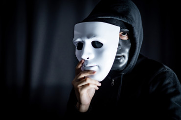 Mystery hoody man wearing black mask holding white mask. Anonymous social masking. Major depressive disorder or bipolar disorder. Halloween concept