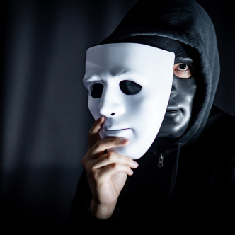 Mystery hoody man wearing black mask holding white mask. Anonymous social masking. Major depressive disorder or bipolar disorder. Halloween concept